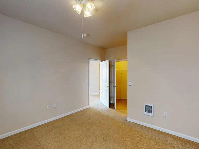 Spacious apartment bedroom with large closet and plush carpet flooring.