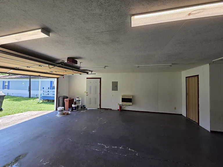 2 car garage with garage door and exit door as well as propane space heater and half bath in background. Garage door is electrical for opening and closing