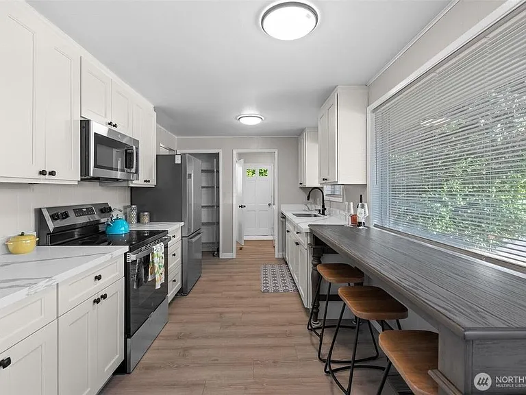 Galley kitchen with ample white cabinetry, full appliance suite, and a window-side breakfast bar for casual meals.