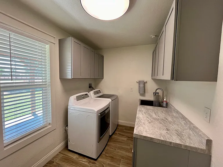 Newly installed laundry room with new cabinets, counter space, laundry sink and new appliances. New lights, window and blinds as well.