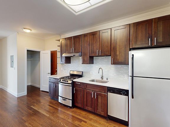 Modern kitchen featuring wood cabinets, stainless steel appliances, and an open layout with a hardwood floor. Bright and inviting space.