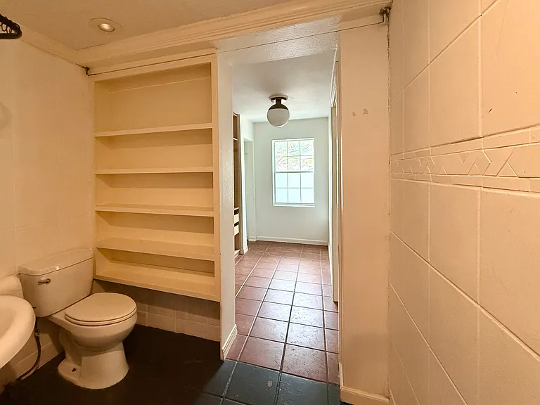 Build in storage in the bathroom next to toilet; this photo was taken with the sink at rear, looking back into the oversized closet / dressing area in the primary suite with door to the entire combined area on R.