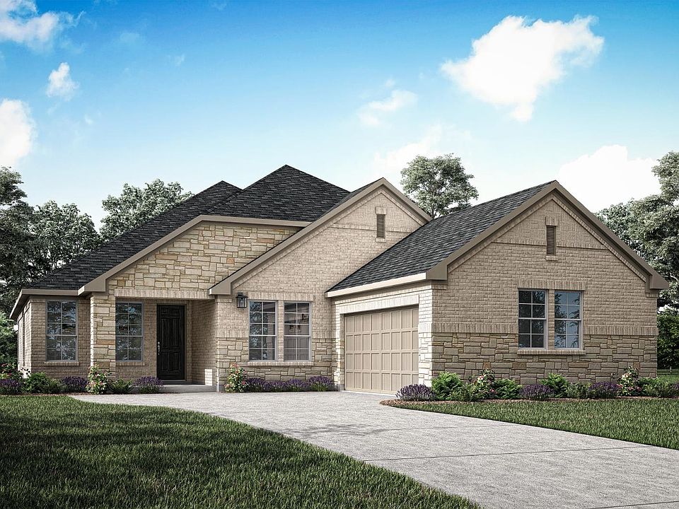 A two-story brick house with a gabled roof, surrounded by lush greenery and a clear blue sky with fl