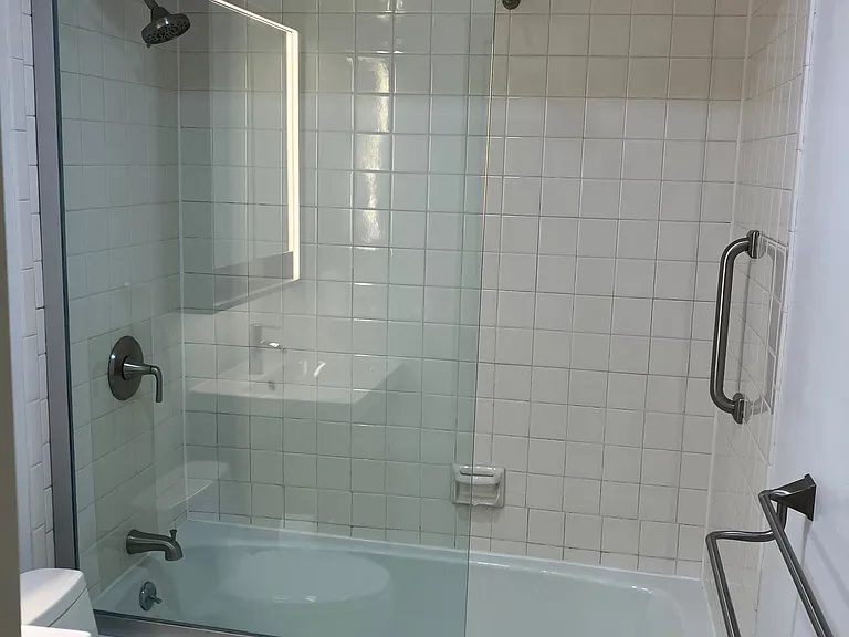 Bathroom with glass shower panel, grab bar, double towel rack and overhead towel storage