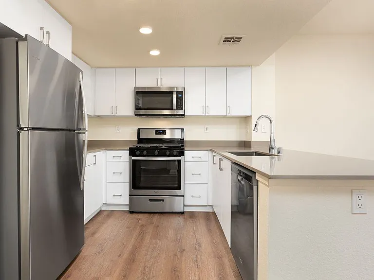 Renovated Package I kitchen with stainless steel appliances, grey quartz countertops, white flat cabinetry, and hard surface flooring