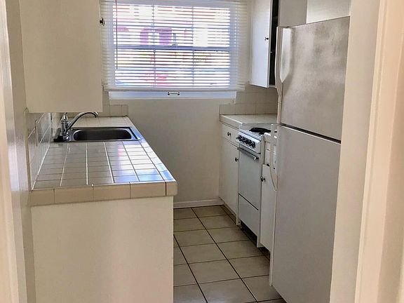 Tiled kitchen with appliances: Stove, fridge/freeze, Dishwasher, garbage disposal.