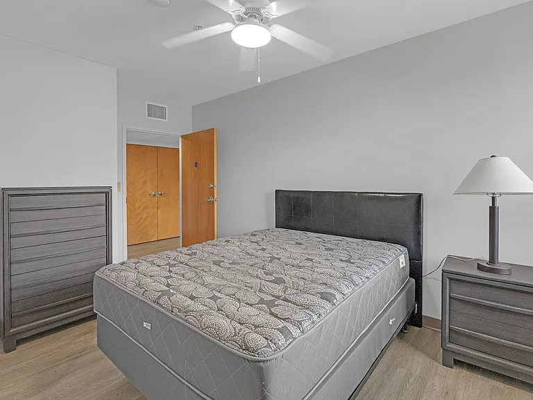 Furnished bedroom with a bed, nightstand, dresser, and ceiling fan, plus convenient access to a closet area.