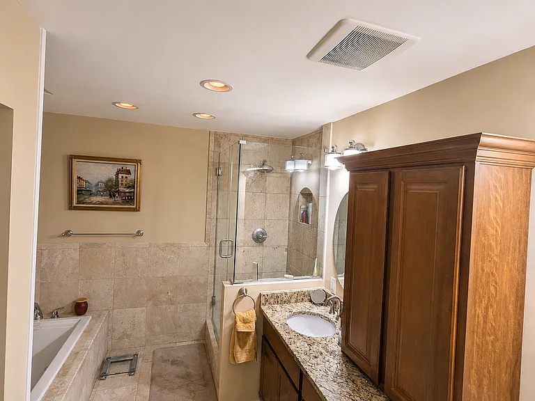 Renovated spa-inspired bathroom with a travertine walk-in shower, soaking tub, and dual granite vanities.