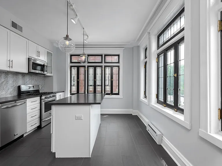 York House designer kitchen with gas stove, quartz countertops, stainless steel appliances, marble kitchen backsplash, and slate tile floor.