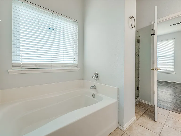Soaking tub with chrome fixtures and overhead window with blinds