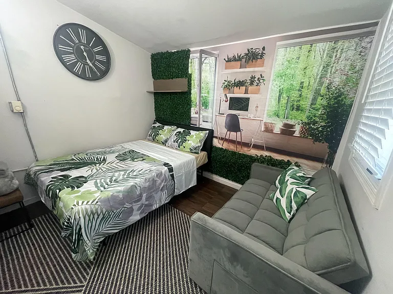 Furnished bedroom with full bed, sofa seating, and window blinds, featuring wood-look floors and stylish accent decor.