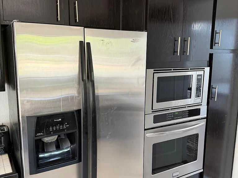 Kitchen features stainless steel side-by-side fridge, built-in microwave and oven, and ample dark cabinetry for storage.