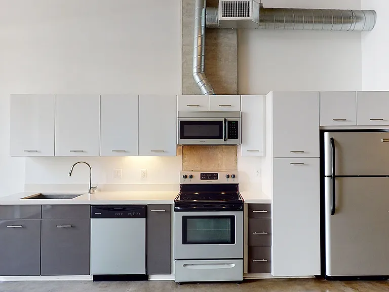Apartment kitchen with stainless steel appliances, quartz countertops and polished concrete flooring.