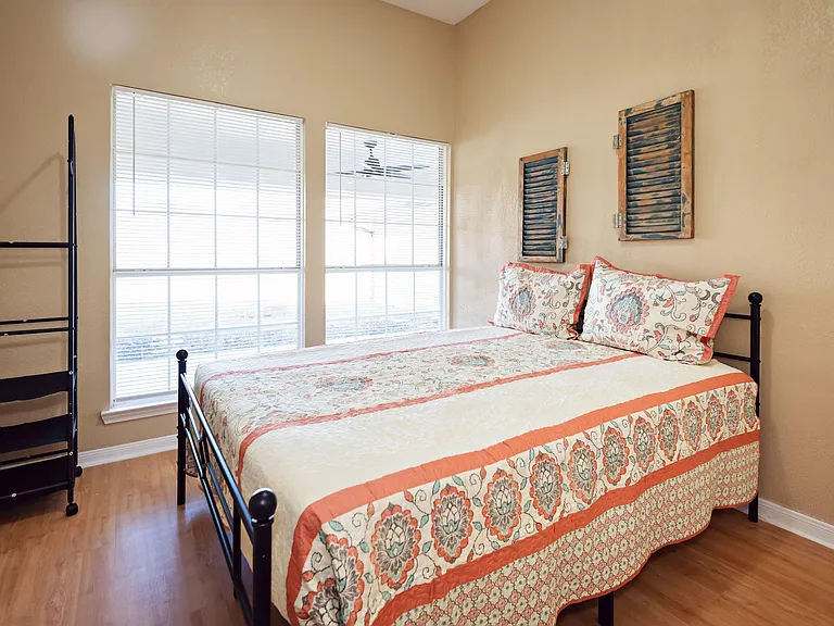 Furnished bedroom with a full-size bed, wood-look flooring, and two large windows with blinds for natural light.