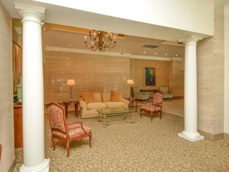 Spacious lobby-style living area with seating groups, elegant columns, chandelier lighting, and plush carpet underfoot.