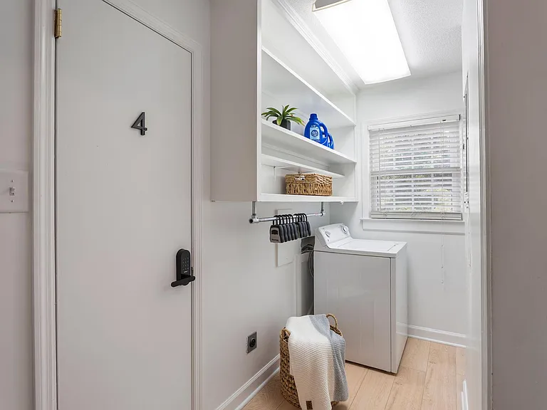 Dedicated laundry nook with built-in shelving, hanging space, and a washer, plus a window for ventilation and light.