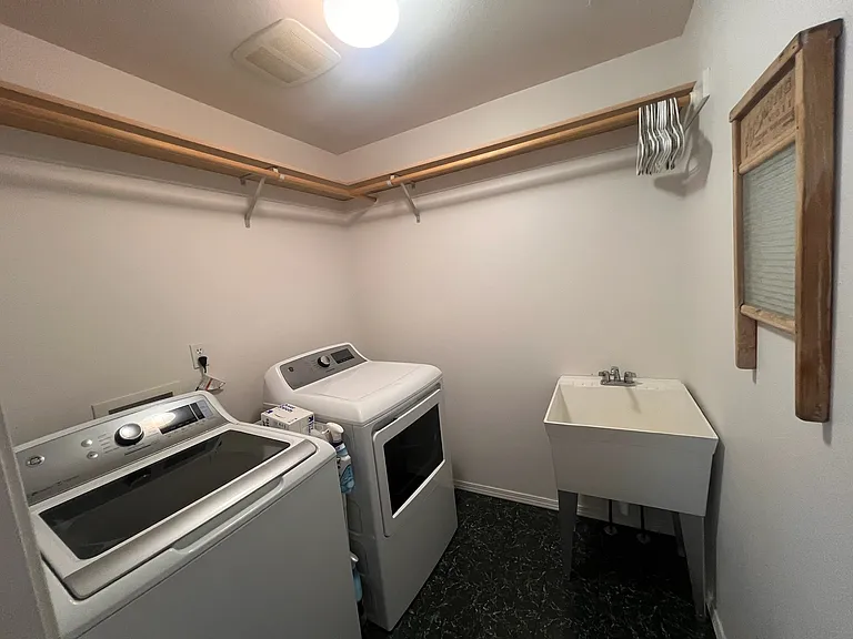 Large laundry room with washer, dryer, sink, hanging racks and shelves