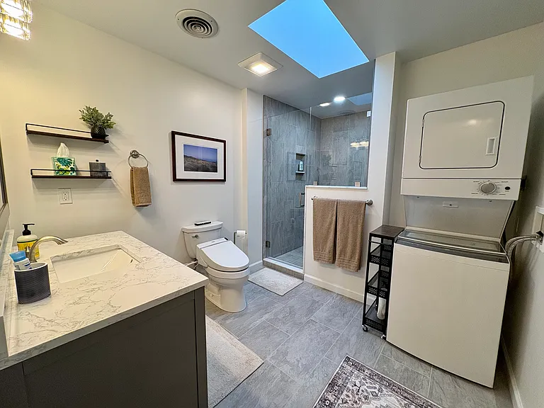 Bathroom features a Japanese toilet with heated seat and bidet, a luxuriously large tile shower, marble vanity, skylight, and a washer and dryer.