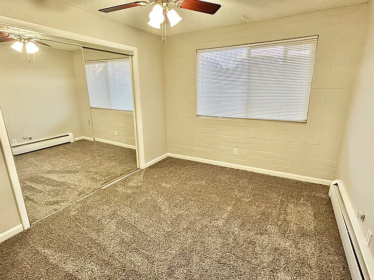 Bright bedroom with plush carpet, mirrored closet doors, and ceiling fan, perfect for relaxation and comfort.