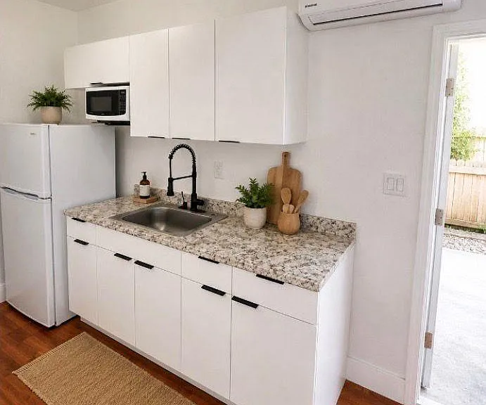 Streamlined kitchen with stone-look counters, deep sink and gooseneck faucet, plus fridge, microwave and ample cabinetry.