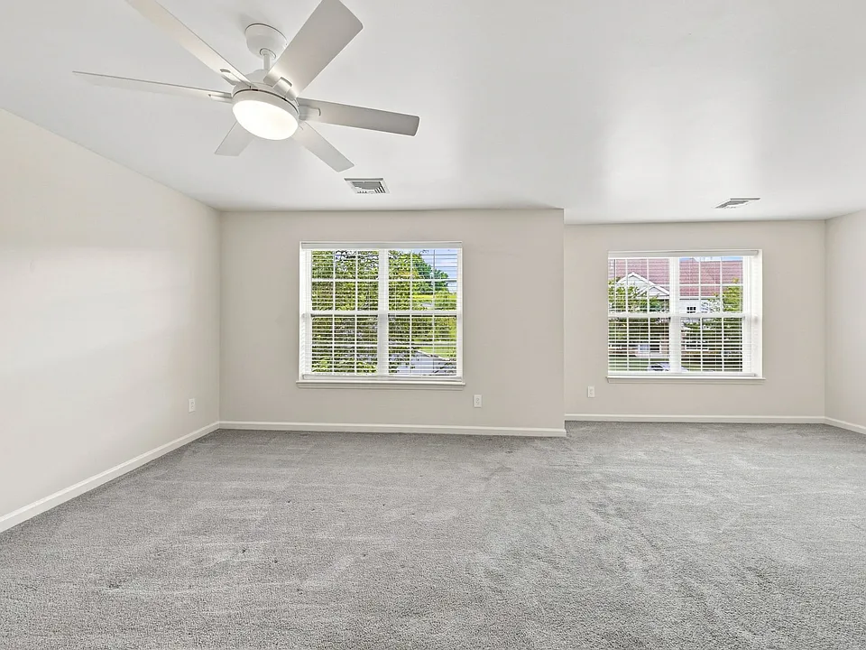 Spacious primary bedroom with two windows, abundant natural light and a modern ceiling fan.