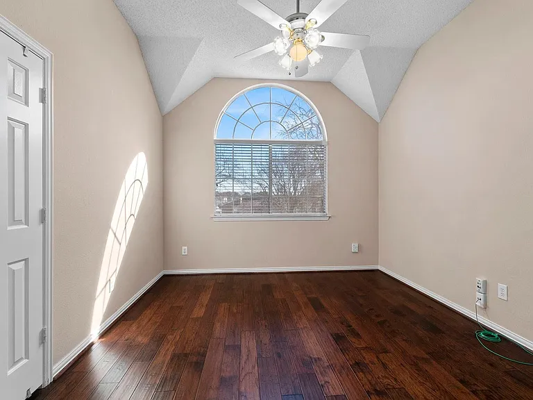 Room featuring an arched window with blinds, dark wood-finish flooring, and a ceiling fan with light fixture
