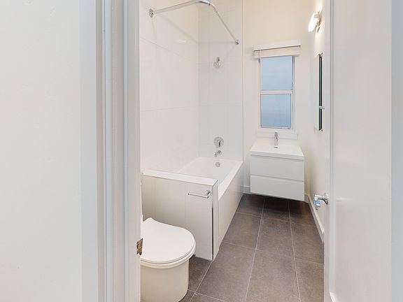 Bathroom featuring a bathtub, toilet, sleek storage vanity, and a window providing natural light, neutral color palette