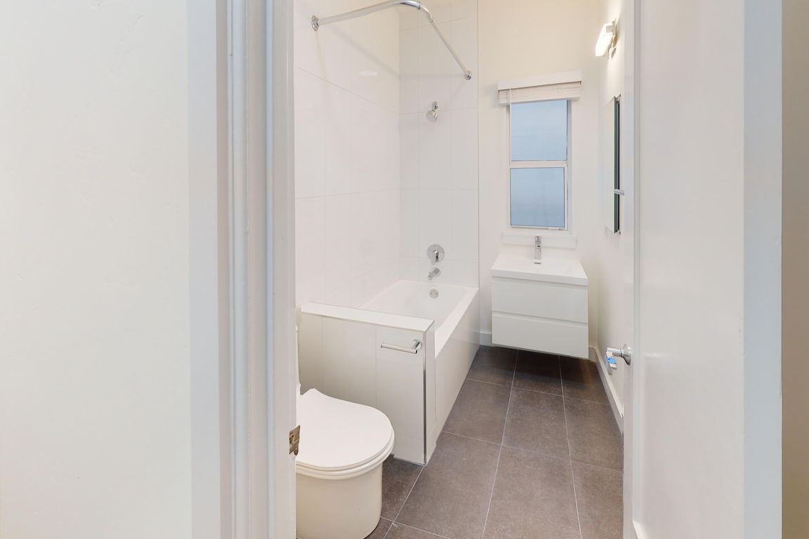 Bathroom featuring a bathtub, toilet, sleek storage vanity, and a window providing natural light, neutral color palette