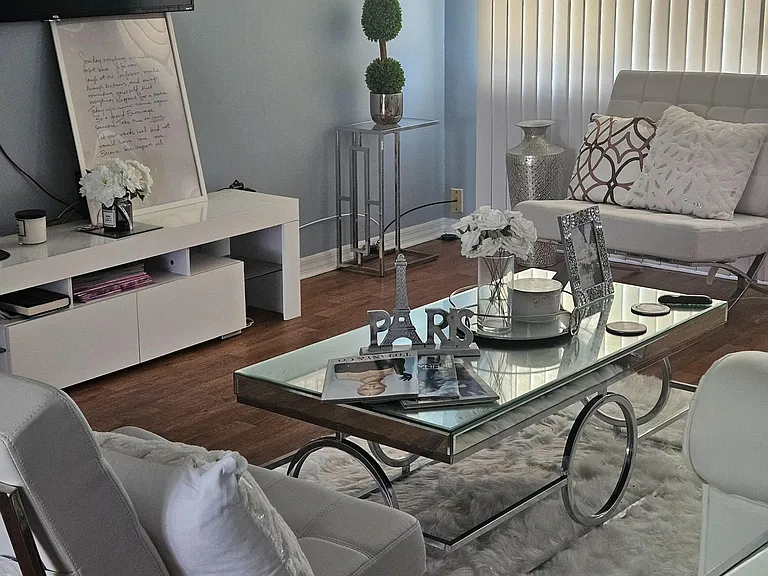 Living room with comfortable seating, a wall-mounted TV, and a glass coffee table, plus window blinds for light control.