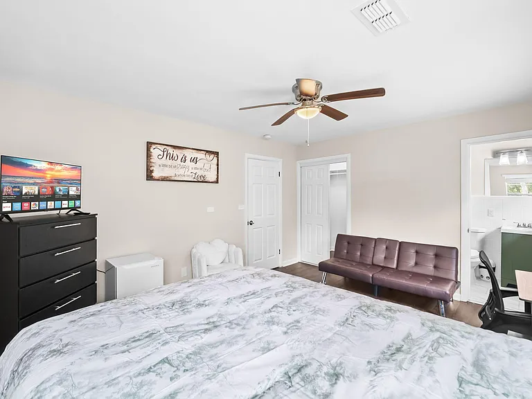 Furnished bedroom with ceiling fan, dresser and TV, plus a desk area and convenient access to an en-suite bath.