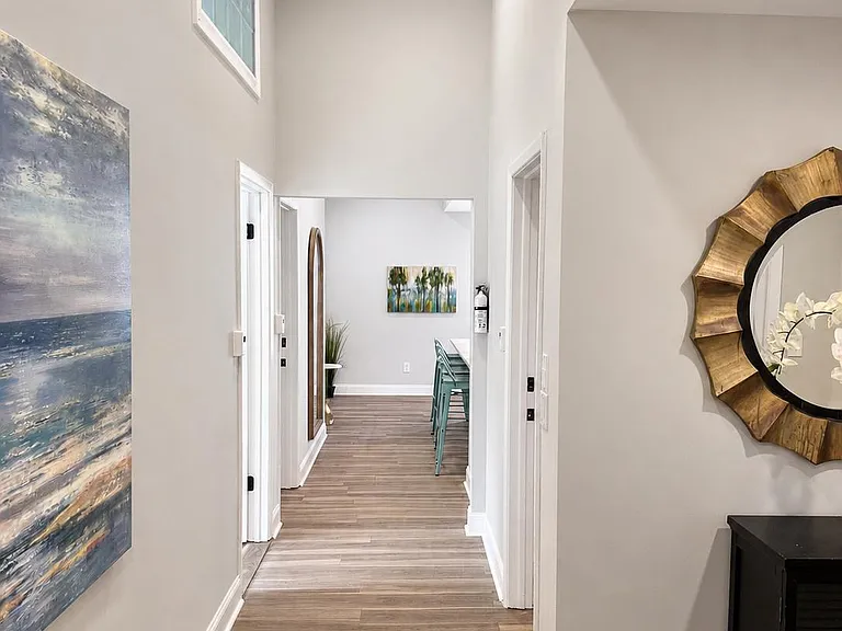 Tall-ceiling hallway with wood-look flooring, multiple doors for easy access, and an open sightline to the kitchen area.