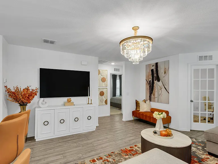 Spacious living area with wood-look floors, a media console and TV, statement chandelier, and flexible seating space.