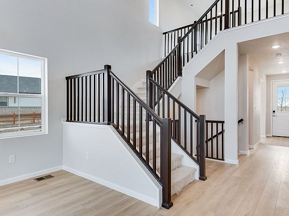 The image shows a modern, open-concept interior with a wooden staircase featuring black metal railin