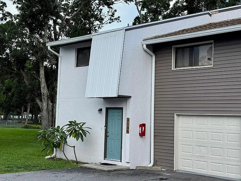 Charming townhouse corner with modern siding, inviting teal door, and lush greenery.