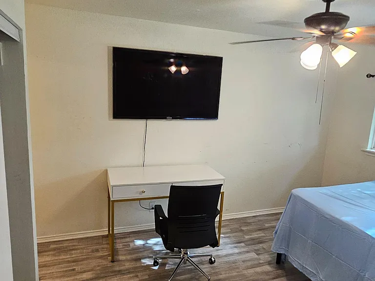 Private bedroom with wood-look flooring, ceiling fan, mounted TV, and dedicated desk space for work or study.