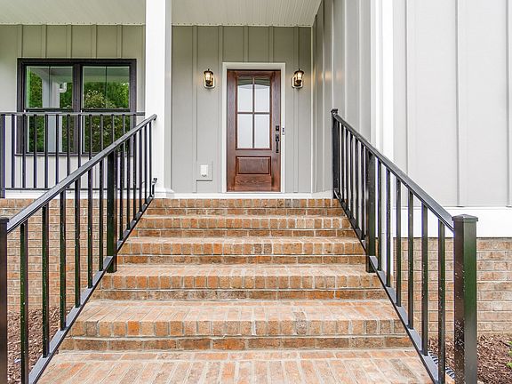 Brick steps with black railings lead to a wooden front door with glass panels on a light gray house.