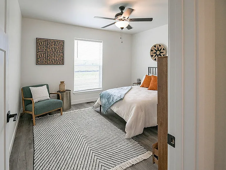 Inviting bedroom with modern decor, featuring a cozy bed with white linens, stylish armchair, and bright window for natural light.