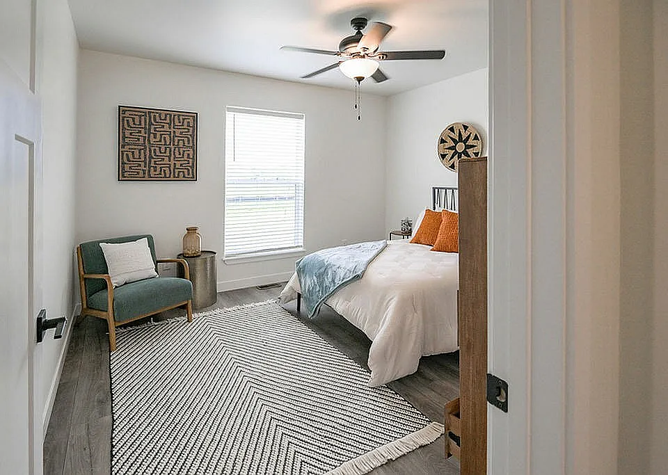 Inviting bedroom with modern decor, featuring a cozy bed with white linens, stylish armchair, and bright window for natural light.