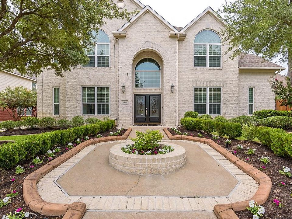 A grand entrance leads to the double front doors and all white brick home. The walk is lined with shrubs and flowers and a well manicured lawn.