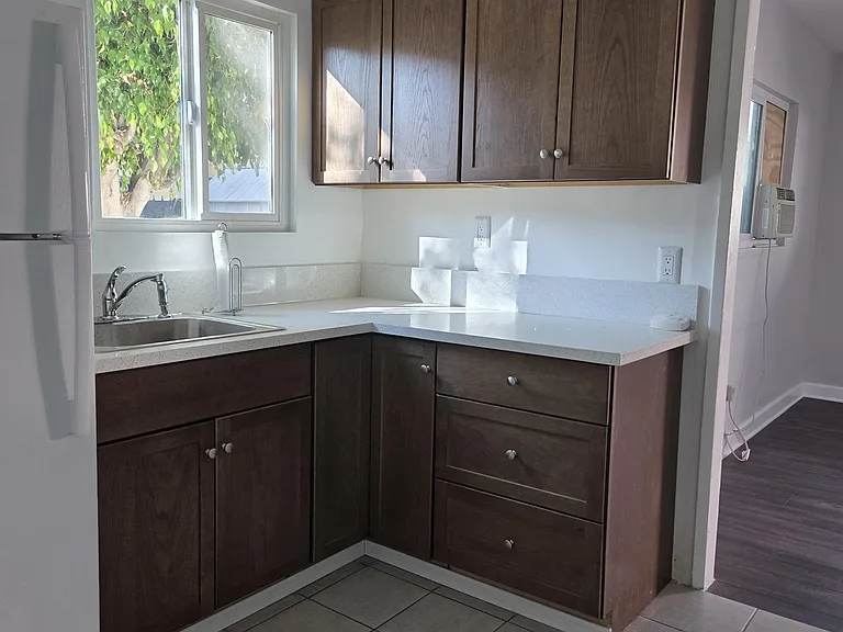 Kitchen with newly installed cabinets and counter top also includes a white refrigerator and stove. Kitchen window has new blinds. (Blinds not shown)