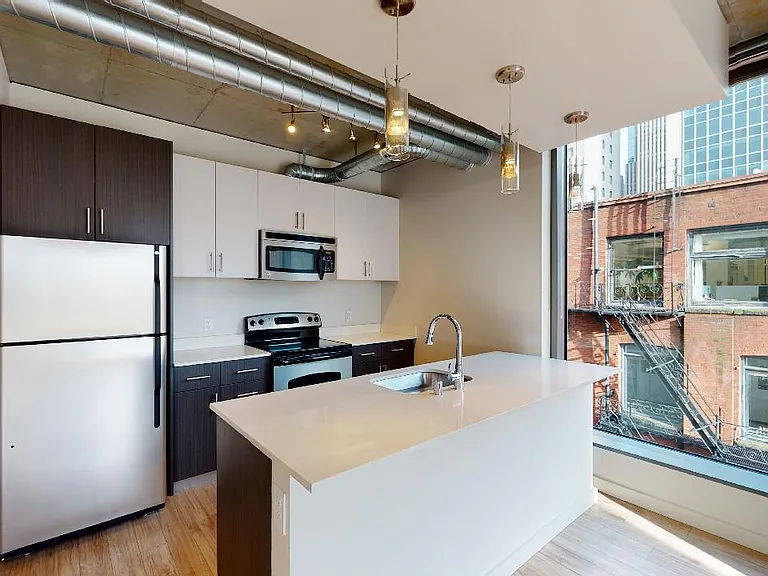 Apartment kitchen with stainless steel appliances, quartz countertops and wood-style flooring.