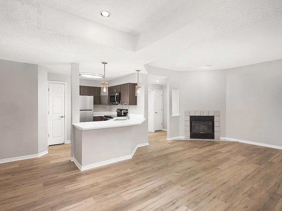 Modern apartment kitchen with elegant white countertops, stainless steel appliances, and warm wood flooring.