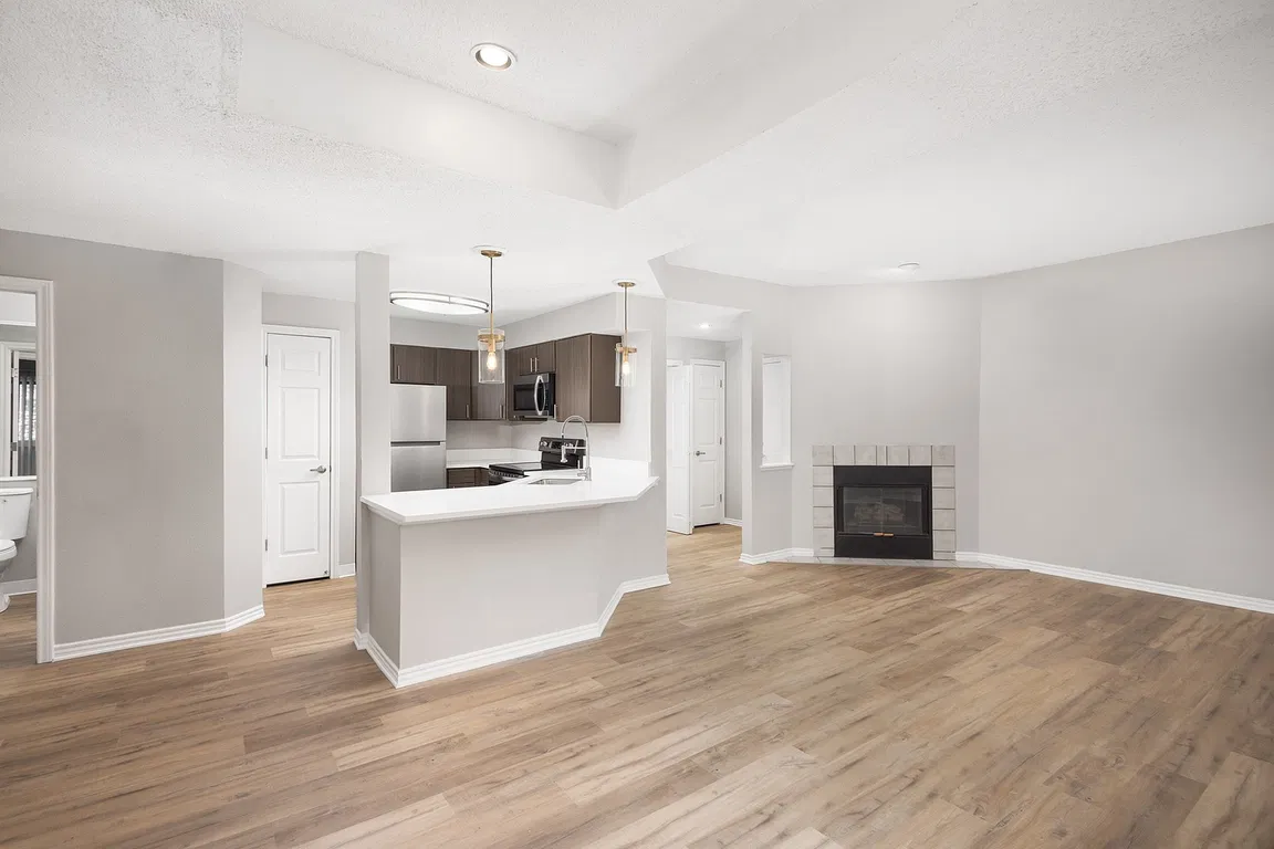 Modern apartment kitchen with elegant white countertops, stainless steel appliances, and warm wood flooring.