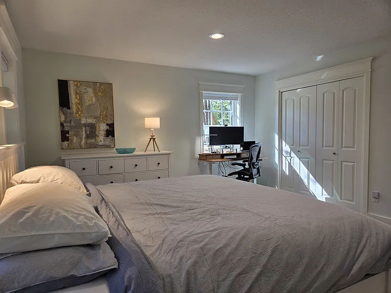 Master suite on the first floor featuring king bed, a 65" TV, and sit-or-stand computer desk with a wide curved monitor