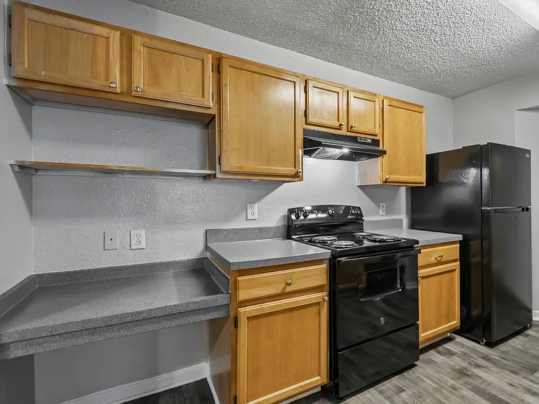 Kitchen with black appliances, wood cabinetry, spacious countertops, and built-in shelving in a 3-bedroom, 2-bath apartment at Gregory Cove in Jacksonville, FL.