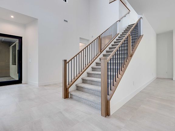 A modern, minimalist staircase with wooden handrails and metal balusters stands in a bright, open sp