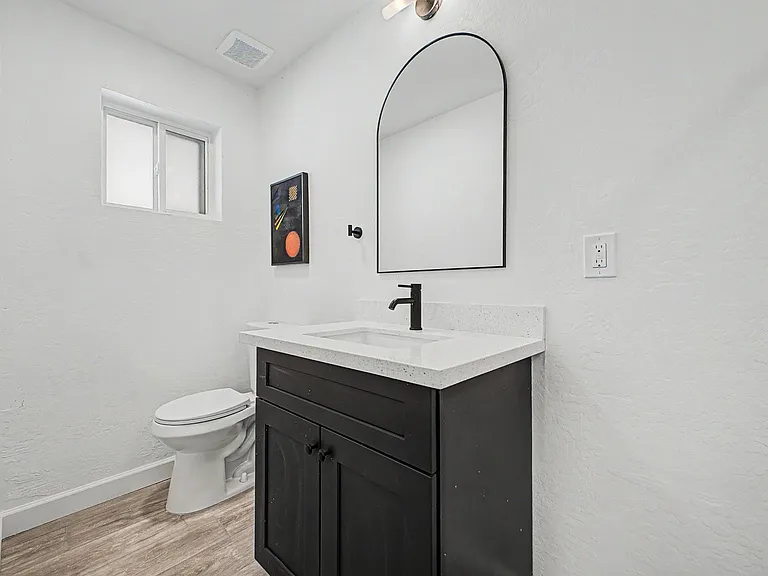 Clean bathroom with a single-sink vanity, arched mirror, and a privacy window for natural light and ventilation.