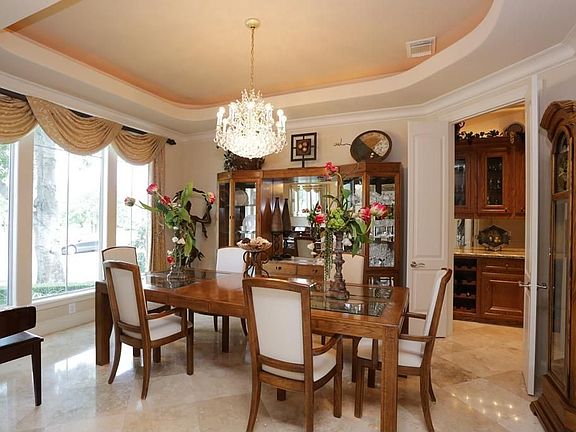 Stunning dining room with those same dramatic stone floors, a trey ceiling with lighting above, crown molding and double doors leading to a butlers pantry.