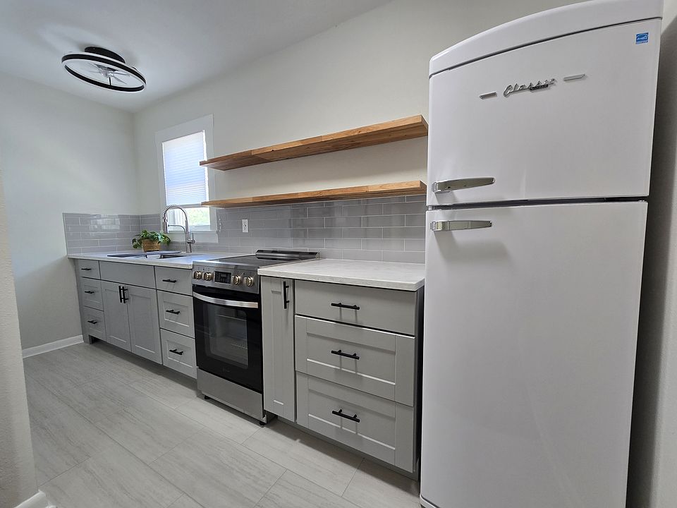 Kitchen with maple cabinetry and floating shelves, electric stove/oven/air fryer, refrigerator, quartz countertops