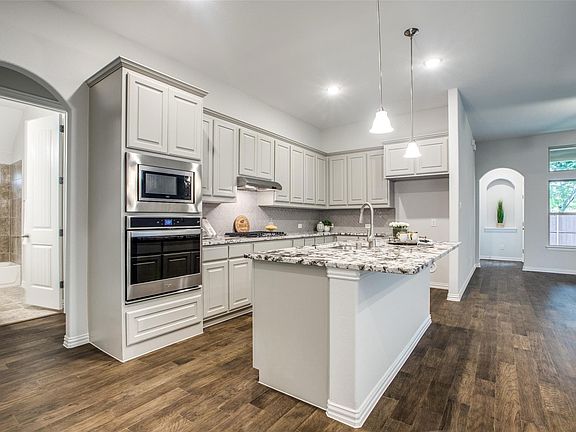 Modern kitchen featuring white cabinetry, stainless steel built-in appliances, a central island with a multi-tone countertop, and wood-finish flooring